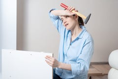 Το πορτρέτο μιας κουρασμένης γυναίκας brunette με ένα σφυρί στα χέρια της, σκουπίζει το μέτωπό της με τον ιδρώτα, συνέλευση επίπλ στοκ φωτογραφία με δικαίωμα ελεύθερης χρήσης Το πορτρέτο μιας κουρασμένης γυναίκας brunette με ένα σφυρί στα χέρια της, σκουπίζει το μέτωπό της με τον ιδρώτα, συνέλευση επίπλ στοκ φωτογραφία με δικαίωμα ελεύθερης χρήσης