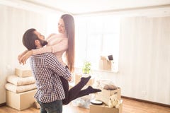 Το όμορφο ζεύγος στέκεται σε ένα φωτεινό δωμάτιο με τα ανοιγμένα κιβώτια Ο νεαρός άνδρας κρατά την ελκυστική σύζυγό του στα χέρια στοκ εικόνα Το όμορφο ζεύγος στέκεται σε ένα φωτεινό δωμάτιο με τα ανοιγμένα κιβώτια Ο νεαρός άνδρας κρατά την ελκυστική σύζυγό του στα χέρια στοκ εικόνα