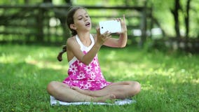 Το όμορφο κορίτσι κάθεται στη χλόη και κάνει selfie στο smartphone του φιλμ μικρού μήκους Το όμορφο κορίτσι κάθεται στη χλόη και κάνει selfie στο smartphone του φιλμ μικρού μήκους
