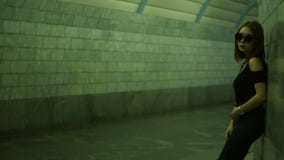 Το όμορφο μοντέρνο κορίτσι στα γυαλιά στέκεται σε μια για τους πεζούς υπόγεια διάβαση κοντά στον τοίχο φιλμ μικρού μήκους Το όμορφο μοντέρνο κορίτσι στα γυαλιά στέκεται σε μια για τους πεζούς υπόγεια διάβαση κοντά στον τοίχο φιλμ μικρού μήκους