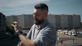 Το όμορφο νέο γενειοφόρο άτομο στέκεται και μιλά στο τηλέφωνο και εξετάζει το ρολόι στην πόλη φιλμ μικρού μήκους Το όμορφο νέο γενειοφόρο άτομο στέκεται και μιλά στο τηλέφωνο και εξετάζει το ρολόι στην πόλη φιλμ μικρού μήκους