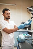 Τομέας εστιάσεως τις σε όλες οδοντικές ανάγκες και τις επιθυμίες σας Νέος οδοντίατρος που κοιτάζει μακριά στεμένος στο γραφείο το στοκ εικόνα Τομέας εστιάσεως τις σε όλες οδοντικές ανάγκες και τις επιθυμίες σας Νέος οδοντίατρος που κοιτάζει μακριά στεμένος στο γραφείο το στοκ εικόνα