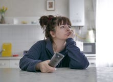 Τρυπημένη νέα συνεδρίαση γυναικών με τον τηλεχειρισμό σχετικά με ένα θολωμένο υπόβαθρο της κουζίνας στοκ εικόνες Τρυπημένη νέα συνεδρίαση γυναικών με τον τηλεχειρισμό σχετικά με ένα θολωμένο υπόβαθρο της κουζίνας στοκ εικόνες