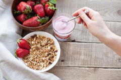 Υγιές πρόγευμα Muesli και γιαούρτι με τις φράουλες Ένα χέρι γυναικών ` s βάζει μια κουταλιά του γιαουρτιού στο muesli στοκ εικόνα με δικαίωμα ελεύθερης χρήσης Υγιές πρόγευμα Muesli και γιαούρτι με τις φράουλες Ένα χέρι γυναικών ` s βάζει μια κουταλιά του γιαουρτιού στο muesli στοκ εικόνα με δικαίωμα ελεύθερης χρήσης