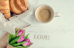 Φλιτζάνι του καφέ με τα croissants, την ανθοδέσμη των ρόδινων τουλιπών και την ξύλινη ΑΓΑΠΗ λέξης Στοκ Εικόνα Φλιτζάνι του καφέ με τα croissants, την ανθοδέσμη των ρόδινων τουλιπών και την ξύλινη ΑΓΑΠΗ λέξης Στοκ Εικόνα