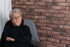 Φτωχή ηλικιωμένη συνεδρίαση γυναικών στην καρέκλα κοντά στο τουβλότοιχο στοκ εικόνα Φτωχή ηλικιωμένη συνεδρίαση γυναικών στην καρέκλα κοντά στο τουβλότοιχο στοκ εικόνα