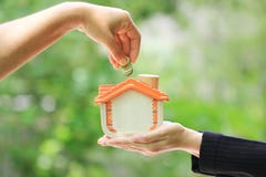 Χέρι γυναικών που βάζει ένα νόμισμα στο ξύλινο σπίτι στη φυσική πράσινη ΤΣΕ στοκ φωτογραφίες με δικαίωμα ελεύθερης χρήσης Χέρι γυναικών που βάζει ένα νόμισμα στο ξύλινο σπίτι στη φυσική πράσινη ΤΣΕ στοκ φωτογραφίες με δικαίωμα ελεύθερης χρήσης