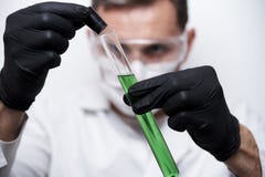 Χέρια ενός επιστήμονα στα μαύρα γάντια που κρατά έναν σωλήνα δοκιμής με ένα επικίνδυνο πράσινο χημικό υγρό στοκ φωτογραφία με δικαίωμα ελεύθερης χρήσης Χέρια ενός επιστήμονα στα μαύρα γάντια που κρατά έναν σωλήνα δοκιμής με ένα επικίνδυνο πράσινο χημικό υγρό στοκ φωτογραφία με δικαίωμα ελεύθερης χρήσης