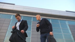 Χαμηλή άποψη γωνίας δύο ευτυχών νέων επιχειρηματιών με τον αστείο χορό χαρτοφυλάκων περπατώντας μετά από την επιτυχή επιχειρησιακ απόθεμα βίντεο Χαμηλή άποψη γωνίας δύο ευτυχών νέων επιχειρηματιών με τον αστείο χορό χαρτοφυλάκων περπατώντας μετά από την επιτυχή επιχειρησιακ απόθεμα βίντεο