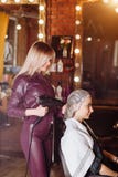 Χαμογελώντας συμπαθητικός επαγγελματικός κομμωτής που συνεργάζεται με το θηλυκό πελάτη που κρατά τον επαγγελματικό στεγνωτήρα τρί στοκ φωτογραφία με δικαίωμα ελεύθερης χρήσης Χαμογελώντας συμπαθητικός επαγγελματικός κομμωτής που συνεργάζεται με το θηλυκό πελάτη που κρατά τον επαγγελματικό στεγνωτήρα τρί στοκ φωτογραφία με δικαίωμα ελεύθερης χρήσης