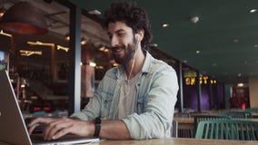 Χαμόγελο blogger χρησιμοποιώντας το lap-top στον πίνακα στον καφέ απόθεμα βίντεο Χαμόγελο blogger χρησιμοποιώντας το lap-top στον πίνακα στον καφέ απόθεμα βίντεο