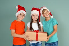 Χαριτωμένα παιδιά στα καπέλα Santa με το κιβώτιο δώρων Χριστουγέννων στο υπόβαθρο χρώματος Στοκ Φωτογραφίες Χαριτωμένα παιδιά στα καπέλα Santa με το κιβώτιο δώρων Χριστουγέννων στο υπόβαθρο χρώματος Στοκ Φωτογραφίες