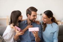 Χαριτωμένες κόρη και σύζυγος που συγχαίρουν το ευτυχές δώρο ανοίγματος πατέρων στοκ εικόνες Χαριτωμένες κόρη και σύζυγος που συγχαίρουν το ευτυχές δώρο ανοίγματος πατέρων στοκ εικόνες