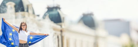 Χαριτωμένο ευτυχές νέο κορίτσι με τη σημαία της Ευρωπαϊκής Ένωσης μπροστά από ένα ιστορικό κτήριο κάπου στην Ευρώπη στοκ εικόνες Χαριτωμένο ευτυχές νέο κορίτσι με τη σημαία της Ευρωπαϊκής Ένωσης μπροστά από ένα ιστορικό κτήριο κάπου στην Ευρώπη στοκ εικόνες