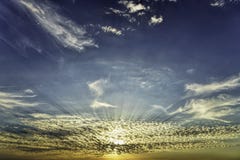 Χρυσές ακτίνες ήλιων ώρας μέσω των όμορφων χαμηλών άσπρων διεσπαρμένων σύννεφων στον πορτοκαλή μπλε ουρανό στοκ εικόνες με δικαίωμα ελεύθερης χρήσης Χρυσές ακτίνες ήλιων ώρας μέσω των όμορφων χαμηλών άσπρων διεσπαρμένων σύννεφων στον πορτοκαλή μπλε ουρανό στοκ εικόνες με δικαίωμα ελεύθερης χρήσης