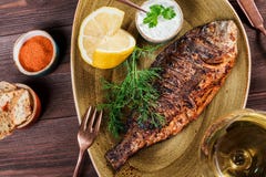 Ψημένα στη σχάρα ψάρια dorado με το λεμόνι και πράσινα στο πιάτο στο ξύλινο υπόβαθρο στοκ φωτογραφία με δικαίωμα ελεύθερης χρήσης Ψημένα στη σχάρα ψάρια dorado με το λεμόνι και πράσινα στο πιάτο στο ξύλινο υπόβαθρο στοκ φωτογραφία με δικαίωμα ελεύθερης χρήσης