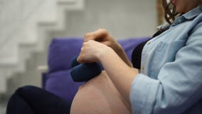 Όμορφη έγκυος νέα γυναίκα που κρατά ένα ζευγάρι των χαριτωμένων καλτσών μωρών γυμνό σε tummy της, που βρίσκεται στο κρεβάτι της σ απόθεμα βίντεο Όμορφη έγκυος νέα γυναίκα που κρατά ένα ζευγάρι των χαριτωμένων καλτσών μωρών γυμνό σε tummy της, που βρίσκεται στο κρεβάτι της σ απόθεμα βίντεο