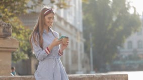 Όμορφη νέα γυναίκα που φορά στο μπλε και άσπρο ριγωτό πουκάμισο φορεμάτων που στέκεται στην παλαιά οδό που χρησιμοποιεί το smartp φιλμ μικρού μήκους Όμορφη νέα γυναίκα που φορά στο μπλε και άσπρο ριγωτό πουκάμισο φορεμάτων που στέκεται στην παλαιά οδό που χρησιμοποιεί το smartp φιλμ μικρού μήκους