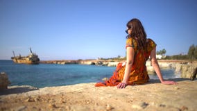 Όμορφη νέα γυναίκα σε μια συνεδρίαση φορεμάτων από τη δύσκολη ακτή στο υπόβαθρο της γραφικής άποψης ενός παλαιού σκάφους, ουρανός απόθεμα βίντεο Όμορφη νέα γυναίκα σε μια συνεδρίαση φορεμάτων από τη δύσκολη ακτή στο υπόβαθρο της γραφικής άποψης ενός παλαιού σκάφους, ουρανός απόθεμα βίντεο