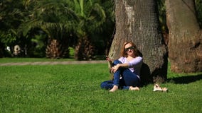 Όμορφη συνεδρίαση γυναικών κάτω από έναν φοίνικα και ξεφύλλισμα του Διαδικτύου σε ένα smartphone φιλμ μικρού μήκους Όμορφη συνεδρίαση γυναικών κάτω από έναν φοίνικα και ξεφύλλισμα του Διαδικτύου σε ένα smartphone φιλμ μικρού μήκους
