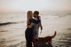 Όμορφο ευτυχές ζεύγος hipster γέλιου νέο με χρυσό retriever στην παραλία ωκεανός μια άμμος Κύματα concepte της ελευθερίας και στοκ φωτογραφία Όμορφο ευτυχές ζεύγος hipster γέλιου νέο με χρυσό retriever στην παραλία ωκεανός μια άμμος Κύματα concepte της ελευθερίας και στοκ φωτογραφία