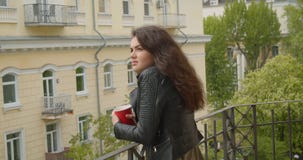 Όμορφο κορίτσι brunette στην προσοχή σακακιών δέρματος στην πράσινη άποψη πόλεων από το μπαλκόνι και το καυτό τσάι κατανάλωσης πο φιλμ μικρού μήκους Όμορφο κορίτσι brunette στην προσοχή σακακιών δέρματος στην πράσινη άποψη πόλεων από το μπαλκόνι και το καυτό τσάι κατανάλωσης πο φιλμ μικρού μήκους