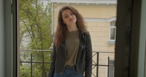 Όμορφο κορίτσι brunette στο σακάκι δέρματος που στέκεται στο μπαλκόνι με την πράσινη άποψη πόλεων που χαμογελά στη κάμερα που είν φιλμ μικρού μήκους Όμορφο κορίτσι brunette στο σακάκι δέρματος που στέκεται στο μπαλκόνι με την πράσινη άποψη πόλεων που χαμογελά στη κάμερα που είν φιλμ μικρού μήκους