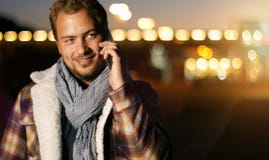 Όμορφος νεαρός άνδρας που μιλά στο έξυπνο τηλέφωνο στο ηλιοβασίλεμα φθινοπώρου στο γ Στοκ Φωτογραφία Όμορφος νεαρός άνδρας που μιλά στο έξυπνο τηλέφωνο στο ηλιοβασίλεμα φθινοπώρου στο γ Στοκ Φωτογραφία