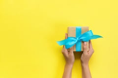 Όπλα γυναικών που κρατούν το κιβώτιο δώρων με την μπλε κορδέλλα στο υπόβαθρο χρώματος, τοπ άποψη στοκ φωτογραφία με δικαίωμα ελεύθερης χρήσης Όπλα γυναικών που κρατούν το κιβώτιο δώρων με την μπλε κορδέλλα στο υπόβαθρο χρώματος, τοπ άποψη στοκ φωτογραφία με δικαίωμα ελεύθερης χρήσης