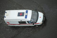 Автомобиль машины скорой помощи идя через затопленную дорогу стоковое изображение Автомобиль машины скорой помощи идя через затопленную дорогу стоковое изображение