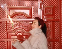Азиатская китайская девушка держа фейерверк бенгальского огня с рукой на фронте красной двери Брюнет, смотря стоковое изображение rf Азиатская китайская девушка держа фейерверк бенгальского огня с рукой на фронте красной двери Брюнет, смотря стоковое изображение rf