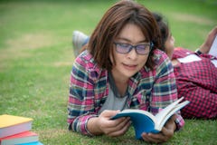 Азиатская книга чтения молодых женщин и друзей на траве снаружи для образования стоковые изображения rf Азиатская книга чтения молодых женщин и друзей на траве снаружи для образования стоковые изображения rf