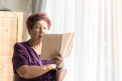 Азиатская старшая женщина читая книгу с светом и годом сбора винограда окна стоковое изображение rf Азиатская старшая женщина читая книгу с светом и годом сбора винограда окна стоковое изображение rf
