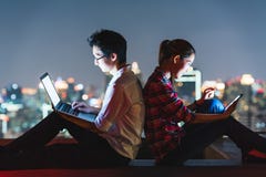 Азиатские пары используя компьтер-книжку и smartphone совместно, полагаются на одине другого на крыше на ноче стоковое фото Азиатские пары используя компьтер-книжку и smartphone совместно, полагаются на одине другого на крыше на ноче стоковое фото