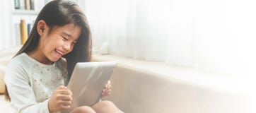 Азиатский милый ребенок играя игры с таблеткой и усмехаясь пока стоковое изображение Азиатский милый ребенок играя игры с таблеткой и усмехаясь пока стоковое изображение