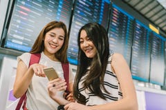 2 азиатских девушки используя smartphone совместно на доске данным по полета в авиапорте Онлайн регистрация, применение расписани стоковые изображения rf 2 азиатских девушки используя smartphone совместно на доске данным по полета в авиапорте Онлайн регистрация, применение расписани стоковые изображения rf