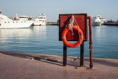 Апельсин lifebuoy на пристани на предпосылке яхт около моря Безопасность на воде и спасении от тонуть стоковая фотография Апельсин lifebuoy на пристани на предпосылке яхт около моря Безопасность на воде и спасении от тонуть стоковая фотография