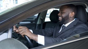 Афро-американский человек сидя в дорогом удовлетворяемом автомобиле и усмехаясь, привод испытания стоковое изображение rf Афро-американский человек сидя в дорогом удовлетворяемом автомобиле и усмехаясь, привод испытания стоковое изображение rf
