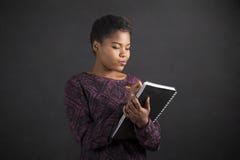 Афро-американское сочинительство женщины в дневнике книги на предпосылке классн классного стоковая фотография rf Афро-американское сочинительство женщины в дневнике книги на предпосылке классн классного стоковая фотография rf