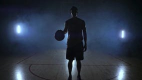 Баскетболист стоит на темной спортивной площадке и держит шарик в его руках и взглядах в камеру в темноте акции видеоматериалы Баскетболист стоит на темной спортивной площадке и держит шарик в его руках и взглядах в камеру в темноте акции видеоматериалы