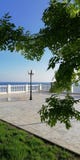 Белая балюстрада прогулки моря через зеленые ветви деревьев Предпосылка лета с настроением праздника стоковое изображение rf Белая балюстрада прогулки моря через зеленые ветви деревьев Предпосылка лета с настроением праздника стоковое изображение rf