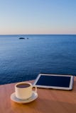 Белое ipad таблетки на столе таблицы с кофейной чашкой, с ландшафтом спокойного моря, дневное время стоковая фотография rf Белое ipad таблетки на столе таблицы с кофейной чашкой, с ландшафтом спокойного моря, дневное время стоковая фотография rf