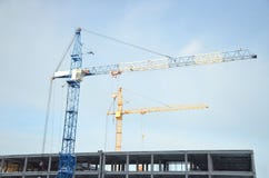 Белые голубые и желтые краны башни возвышаясь над бетонным зданием под конструкцией против голубого неба стоковое изображение rf Белые голубые и желтые краны башни возвышаясь над бетонным зданием под конструкцией против голубого неба стоковое изображение rf