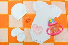 Белый bodysuit, Romper, белая крышка, белые добычи, pacifier и teether Вещи для младенцев в проверенном одеяле стоковое изображение rf Белый bodysuit, Romper, белая крышка, белые добычи, pacifier и teether Вещи для младенцев в проверенном одеяле стоковое изображение rf