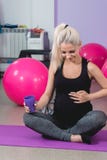 Беременная женщина в спортзале сидя на циновке ослабляя после тренировки для того чтобы держать пригонку себя стоковые изображения Беременная женщина в спортзале сидя на циновке ослабляя после тренировки для того чтобы держать пригонку себя стоковые изображения