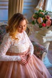 Беременная женщина сидя в красивом платье на кресле Концепция материнства стоковое изображение Беременная женщина сидя в красивом платье на кресле Концепция материнства стоковое изображение