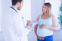 Беременный терпеливый говорить к доктору который принимает примечания стоковая фотография Беременный терпеливый говорить к доктору который принимает примечания стоковая фотография