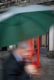 Бизнесмен держа зонтик второпях проходя красное telepho стоковые изображения Бизнесмен держа зонтик второпях проходя красное telepho стоковые изображения