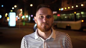 Близкий поднимающий вверх портрет красивого бородатого человека в striped футболке поло на улице ночи с trammy на предпосылке сток-видео Близкий поднимающий вверх портрет красивого бородатого человека в striped футболке поло на улице ночи с trammy на предпосылке сток-видео