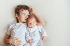 Более старый брат обнимая его newborn сестру Дети в ярких одеждах на белом одеяле стоковое изображение Более старый брат обнимая его newborn сестру Дети в ярких одеждах на белом одеяле стоковое изображение